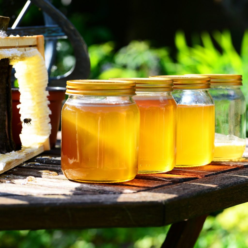 homemade honey in jars on wooden table with honeycomb in background